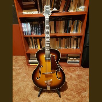 Polodupová elektrická kytara s hnědým sunburst povrchem a f-otvory. Na hlavě je bílý nápis "Parlor". Nástroj má tmavý hmatník, tmavě hnědý pickguard…