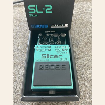 Kytarový efekt Boss SL-2 Slicer v tyrkysovém provedení, umístěný ve své originální černé krabici. Na pedálu jsou viditelné tři ovládací knoflíky a ná…