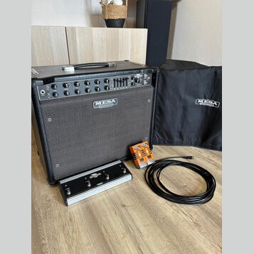 Černý kytarový kombozesilovač s logem MESA ENGINEERING na předním textilním krytu. Před zesilovačem je umístěn stříbrný nožní spínač s nápisy EXPRESS…