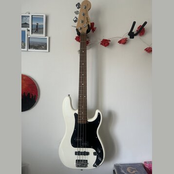 Bílá elektrická basová kytara s černým pickguardem a hnědým hnedým hředníkem. Na hlavě nástroje je viditelné logo Squier. Kytara má dva snímače a čty…