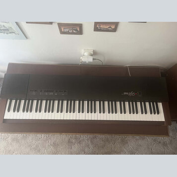 Černý digitální klavír umístěný na hnědém dřevěném stole. Na pravé straně je bílý nápis YAMAHA a vedle něj modelové označení pf15. Nástroj má standar…