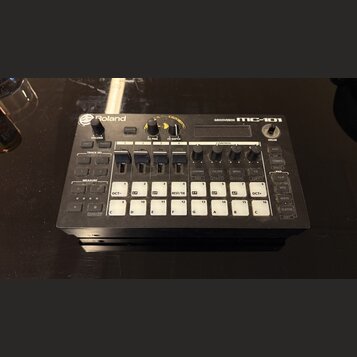 Černá groovebox s bílými popisky a tlačítky. Na horní hraně je nápis Roland vlevo a GROOVEBOX MC-101 vpravo. Zařízení obsahuje několik ovládacích kno…
