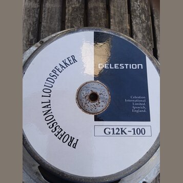 Zadní strana reproduktoru s bílým a tmavě modrým povrchem. Je na ní nápis PROFESSIONAL LOUDSPEAKER a značka CELESTION s označením modelu G12K-100. V…