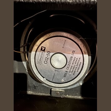 Fotografie zachycuje zadní stranu reproduktoru s kovovým magnetem. Na středovém štítku je uveden název Celestion G12-50 a impedance 8 ohms. Kolem stř…