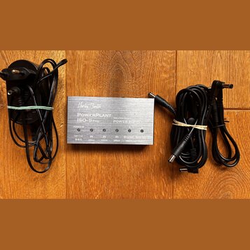 Stříbrný zdroj napájení s nápisy „Harley Benton“, „POWERPLANT ISO-5 PRO“ a „ISOLATED OUTPUTS POWER SUPPLY“. Zařízení má pět výstupů s označením „12V…