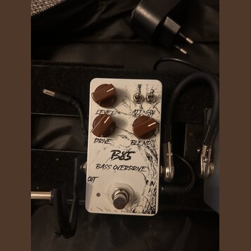 Bílý kytarový efekt s nápisy B85 a BASS OVERDRIVE. Na horní straně jsou tři hnědé otočné knoflíky s popisky LEVEL, DRIVE a BLEND a dva přepínací spín…