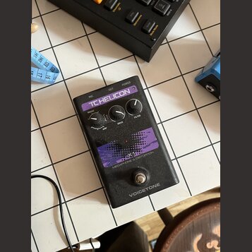 Černý efekt pedál s fialovými grafickými prvky. Na horní části je nápis TC HELICON a v dolní části označení X1 MEGAPHONE & DISTORTION a VOICETONE. Za…