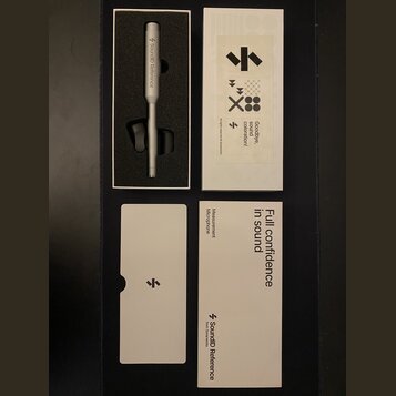 Fotografie zobrazuje stříbrný měřicí mikrofon v originálním bílém balení s doprovodnými dokumenty. Na těle mikrofonu je nápis SoundID Reference s log…