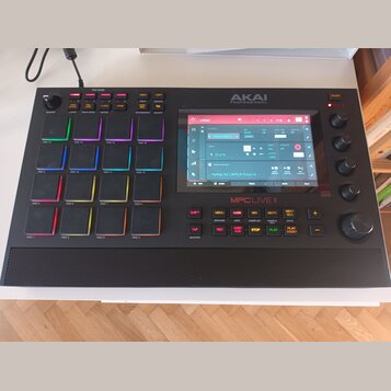 Černý samplovač MPC LIVE II značky AKAI PROFESSIONAL. Zařízení má 16 podsvícených padů, ovládací knoflíky a centrální displej s rozhraním softwaru. N…
