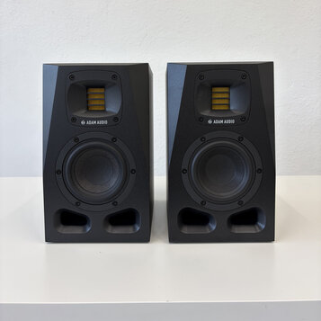 Dva černé studiové monitory značky ADAM AUDIO. Každý reproduktor má v horní části žlutý výškovek a ve spodní části černý basový reproduktor. Povrch j…