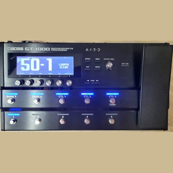 Černý kytarový procesor s nápisem BOSS GT-1000 GUITAR EFFECTS PROCESSOR a označením AIRD. Zařízení má LCD displej, na kterém je zobrazen text P50-1 a…
