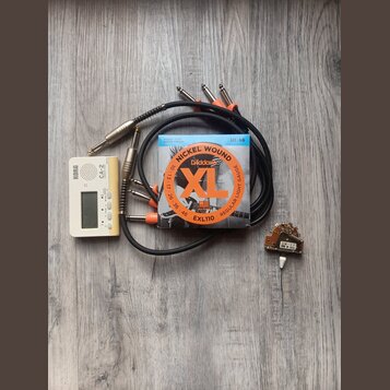 Sada příslušenství složená z bílého ladičky KORG CA-2, balení strun D'Addario XL EXL110 NICKEL WOUND 10-46, černého kabelu s několika konektory a mal…
