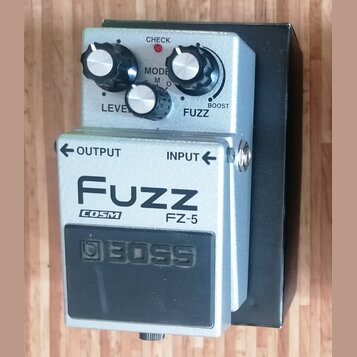 Stříbrný kytarový efekt s černým spínacím pedálem. Na horní části jsou tři ovládací knoflíky a nápisy LEVEL, MODE a FUZZ s možností BOOST. Na přední…