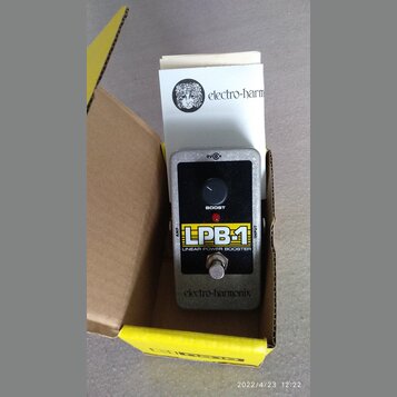 Kytarový efekt v šedém kovovém krytu s černým předním panelem, umístěný v kartonové krabici. Na panelu je nápis LPB-1, LINEAR POWER BOOSTER a BOOST,…