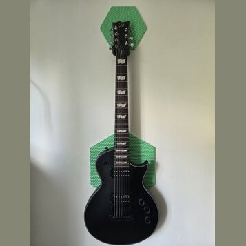Černá elektrická kytara s dvojsečným stupňovitým hmatníkem a dvěma humbuckery. Na hlavě je bílé logo Ltd. Nástroj je umístěn před dvěma zelenými hexa…