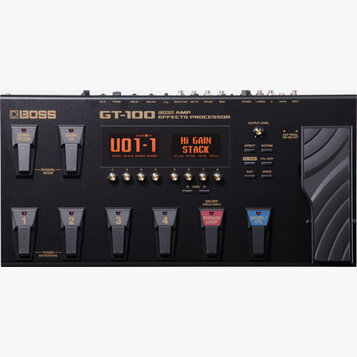 Černý kytarový procesor Boss GT-100 Guitar Amp Effects Processor. Zařízení má digitální displej s nápisem U01-1 a Hi Gain Stack, několik ovládacích k…