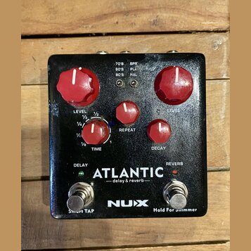 Černý efekt pedál s červenými ovládacími knoflíky. Na spodní části je bílý nápis ATLANTIC — delay & reverb — a logo NUX. Pedál obsahuje dva spínače s…
