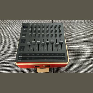 Černý MIDI kontrolér s nápisem LAUNCHCONTROL XL. Horní část obsahuje mřížku šesti řad s otočnými knoflíky, pod nimi je osm posuvníků a v dolní části…