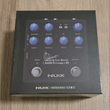Fotografie znázorňuje krabici s basovým předzesilovačem NUX. Na zařízení jsou vidět ovládací knoflíky s popisky VOLUME, BLEND, IR, DRIVE, BASS, MIDDL…
