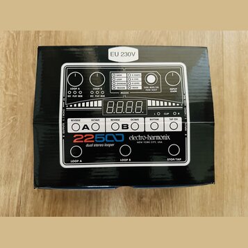 Fotografie znázorňuje krabici s pedalem efektu. Na ní je zobrazen bílý přístroj s nápisy 22500 dual stereo looper a electro-harmonix NEW YORK CITY, U…