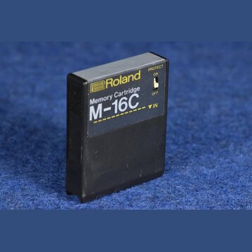 Černá paměťová karta z plastu s žlutými nápisy. Na přední straně je logo a název Roland, text Memory Cartridge a označení modelu M-16C. Na pravém bok…