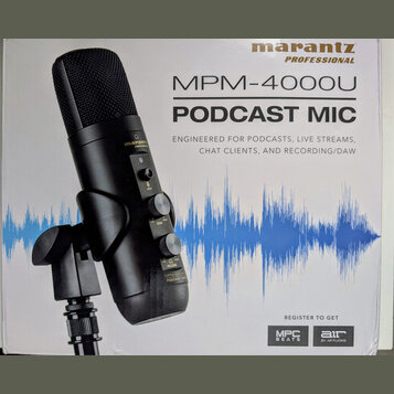 Fotografie znázorňuje krabici s černým kondenzátorovým mikrofonem. Na obalu je uveden název značky marantz PROFESSIONAL a model MPM-4000U PODCAST MIC…