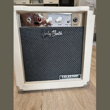 Kytarový kombozesilovač v bílém vinylovém potahu s kovovými rohy. Na předním černém textilním krytu je nápis „Harley Benton“ a v pravém dolním rohu š…