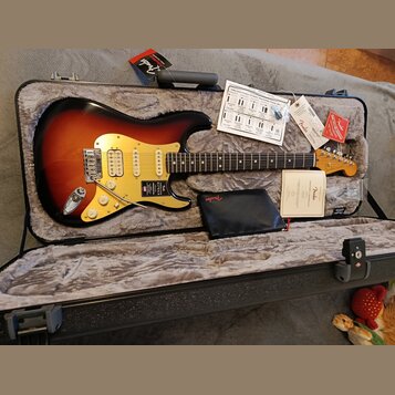 Elektrická kytara typu Stratocaster s barevným přechodem od černé přes červenou k žluté a světlým hmatníkem. Na krytce je nápis „American ULTRA STRAT…