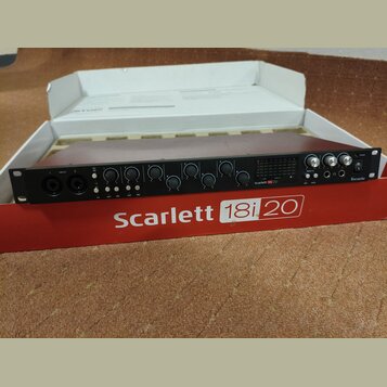 Černý rackový zvukový rozhraní umístěný v původním červenobílém obalu. Na přední straně zařízení je nápis Scarlett 18i20 a logo Focusrite. Přístroj o…