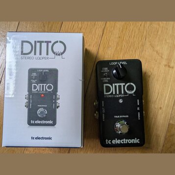 Černý efekt pedál s nápisy DITTO STEREO LOOPER a tc electronic. Na horní části jsou popisky LOOP LEVEL, BACKING TRACK LEVEL a STORE hold to DELETE. V…