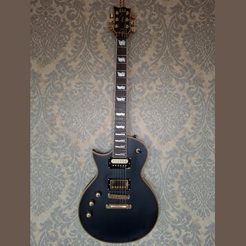 Černá elektrická kytara typu singlecut s hnědým lemováním. Na hlavě je zlaté logo Ltd a nápis ESP. Kytara má dva humbuckery se zlatými kryty, zlatý m…