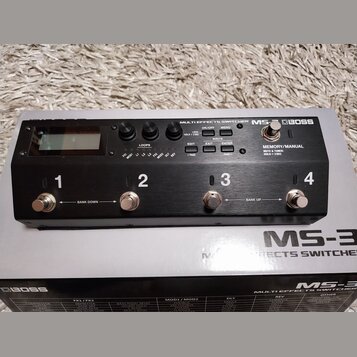 Černý kytarový efektový spínáč Boss MS-3 s kovovým povrchem. Na horní straně je LCD displej, ovládací knoflíky a tlačítka s nápisy LOCK: HOLD > 2 SEC…