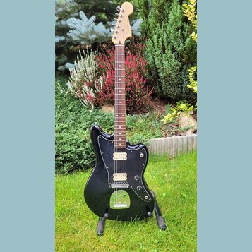 Černá elektrická kytara s tmavým hnedým hmatníkem a světlou hlavou. Na těle je černý pickguard, dva snímače s bílými plastovými krytkami a chromovaný…