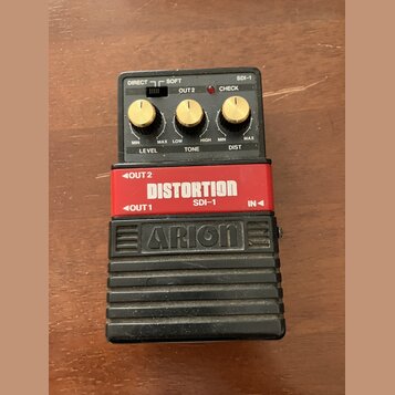 Kytarový efekt pedál s černým spodním tělem a červeným horním panelem. Na červené části je bílý nápis DISTORTION a pod ním SDI-1, v dolní části je vy…