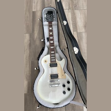 Bílá elektrická kytara s tvarem singlecut v černém etuši s bílou vnitřní výplní. Na hlavě je viditelné logo Gibson. Kytara má dva humbuckery, světle…