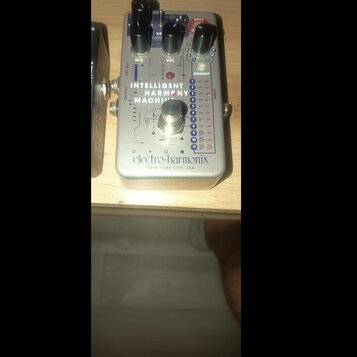 Stříbrný efekt pedál s nápisem INTELLIGENT HARMONY MACHINE a logem electro-harmonix NEW YORK CITY, USA. Na horní straně jsou tři černé otočné ovladač…