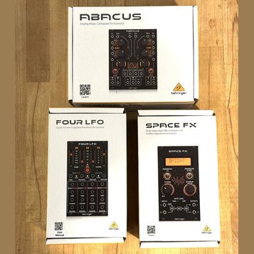 Fotografie zobrazuje tři bílé krabice s moduly pro Eurorack od značky behringer. Horní krabice nese nápis ABACUS Analog Music Computer for Eurorack.…