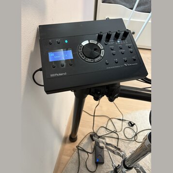 Černý elektronický bicí modul s displejem, na kterém je nápis "KIT 100 User Kit". Na spodní hraně je logo "Roland" a vpravo nápis "DRUM SOUND MODULE…