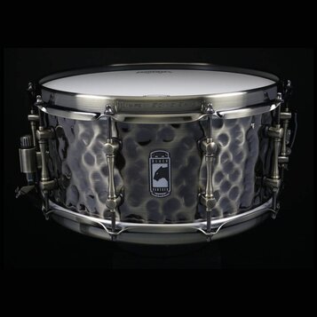Kovový snare drum s tmavým, kovem vypracovaným povrchem v kladeném vzoru. Uprostřed korpusu je logo s panterem a nápisem BLACK PANTHER. Na horním obr…