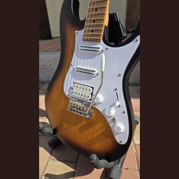 Elektrická kytara s tělem v provedení sunburst a bílým pickguardem. Nástroj má tři snímače typu single-coil, chromovaný most s páčkou a tři bílé ovlá…