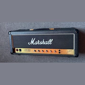 Kytarový zesilovač v černém vinylovém potahu s bílým logem Marshall na předním textilním krytu. Na zlatém ovládacím panelu je nápis JCM 800 LEAD SERI…