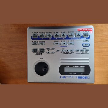 Stříbrný elektronický bicí automat značky BOSS, model Dr. Rhythm DR-3. Zařízení má horní panel s modrými a šedými tlačítky, ovládací knoflík VALUE a…