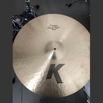 Zlatavý činely s kovaným povrchem. Na horní části je nápis Custom Dark Ride a 22"/56cm, ve spodní části je velké černé logo K. Povrch vykazuje drobné…