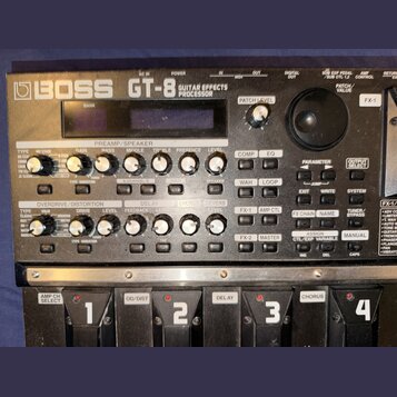 Černý kytarový procesor Boss GT-8 Guitar Effects Processor. Zařízení obsahuje displej, početné otočné knoflíky a tlačítka s nápisy jako PREAMP/SPEAKE…