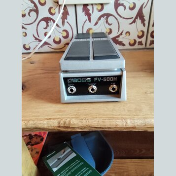 Stříbrný expresní pedál s dvěma šedými plochmi pro nohu. Na zadní straně je nápis BOSS FV-500H a tři konektory označené jako INPUT, OUTPUT a EXP. Pov…