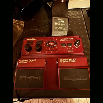 Červený kytarový pedál s nápisy Digitech a HARMONYMAN INTELLIGENT PITCH SHIFTER. Zařízení má dva ovládací knoflíky označené VOICE 1 a VOICE 2, knoflí…