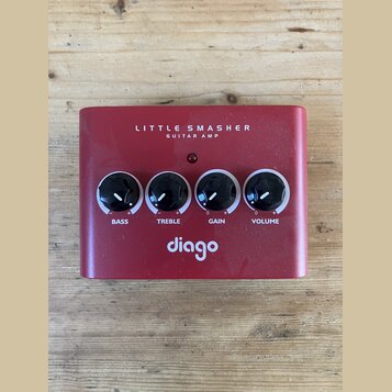 Červený kovový kytarový zesilovač s nápisem LITTLE SMASHER GUITAR AMP a logem diago. Na přední straně jsou čtyři černé otočné ovířky s popisky BASS,…