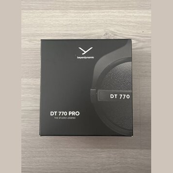 Černá čtvercová krabice s obrázkem sluchátek. Na horní části je bílé logo a nápis beyerdynamic, vpravo je uveden model DT 770. V levém dolním rohu je…
