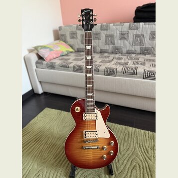 Elektrická kytara s tmelem v červeně-žlutém sunburst provedení a hnědým hmatníkem. Na hlavě je bílý nápis Gibson a pod ním kurzivní nápis Les Paul. N…
