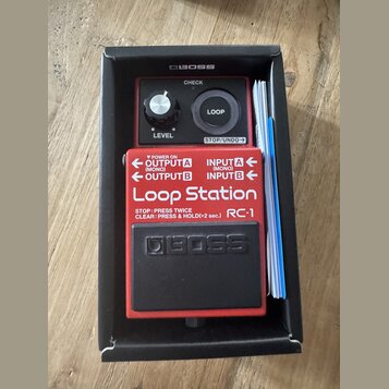Červený kytarový pedál Boss Loop Station RC-1 v originální černé krabici s přiloženou dokumentací. Na horní části je ovládací knoflík LEVEL, tlačítko…